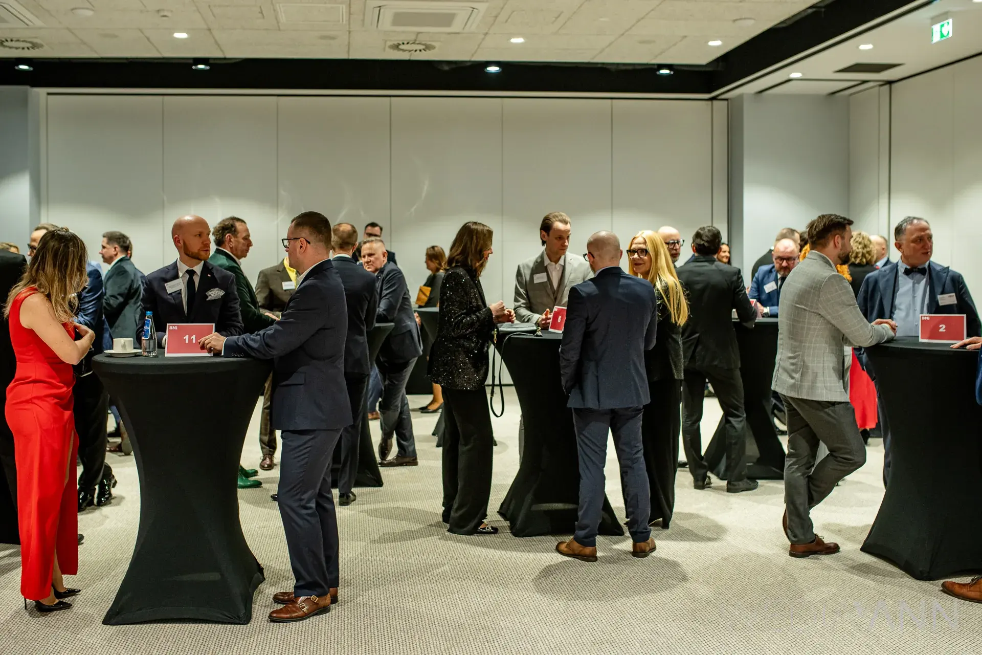 Kilkanaście osób rozmawia przy wysokich stolikach podczas networkingu