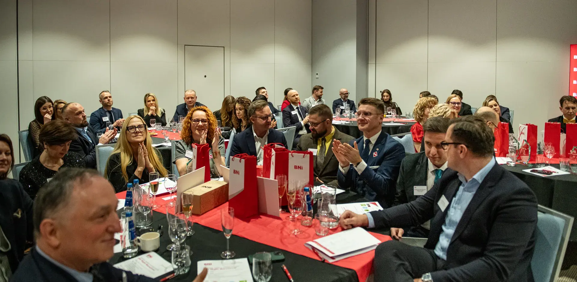 Chapter Members at tables with BNI materials applaud during the weekly meeting