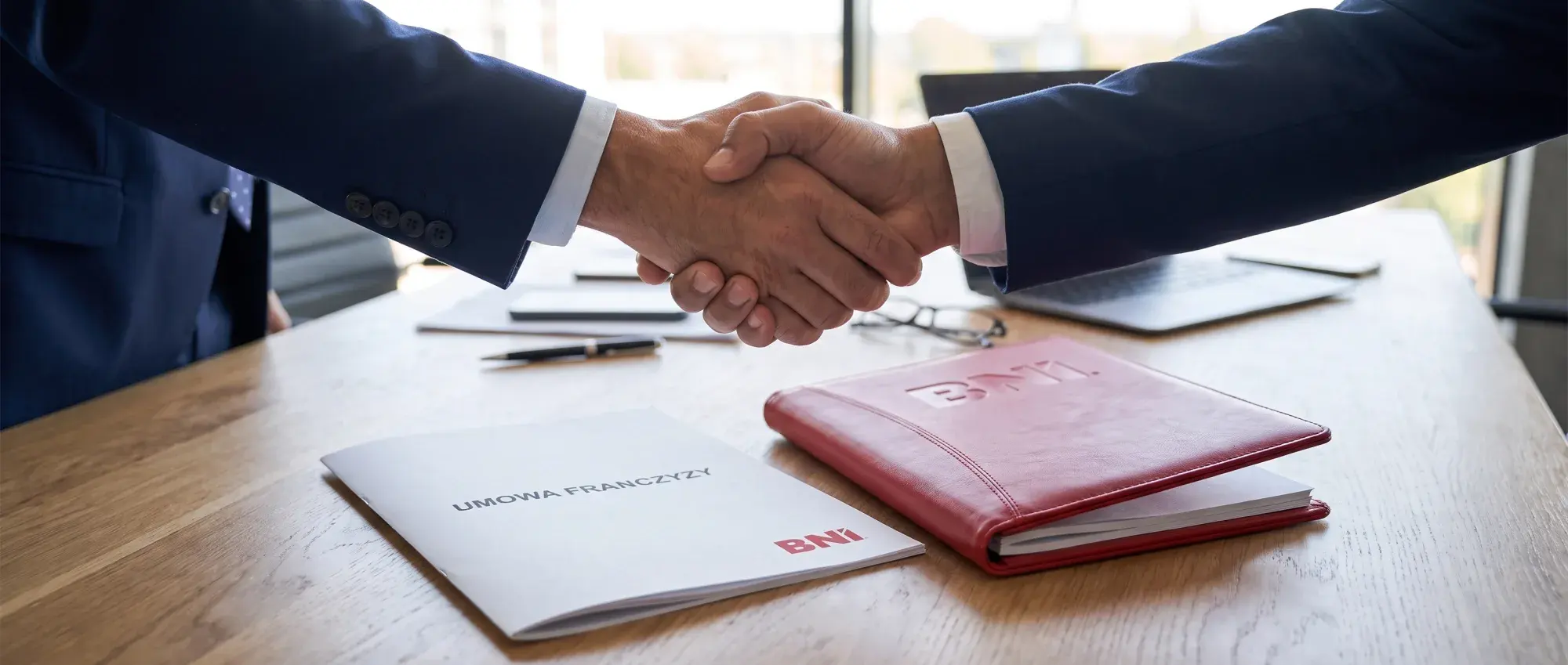 A handshake over documents and a red BNI folder
