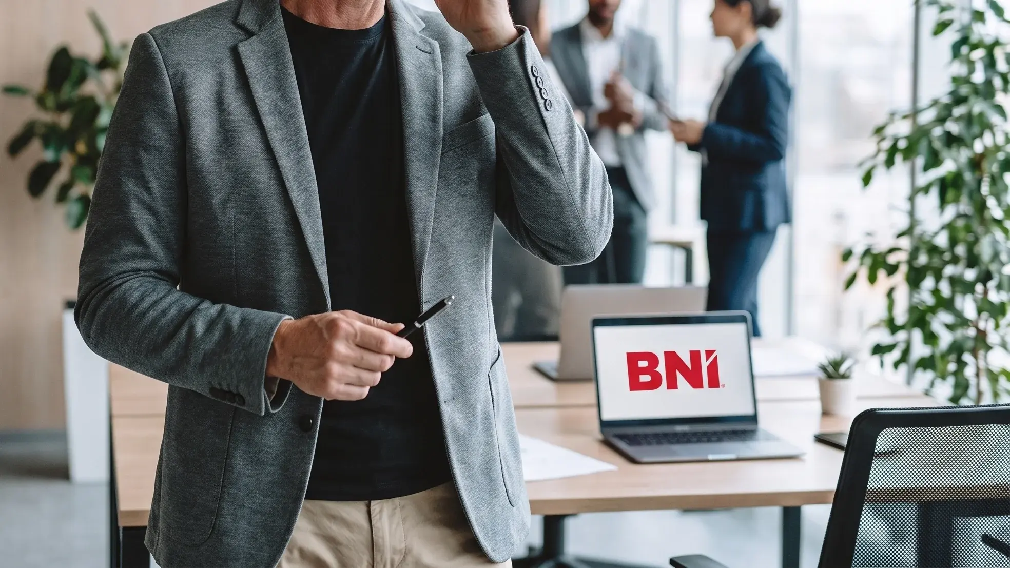 Dłoń z długopisem, w tle laptop z logo BNI w jasnym biurze