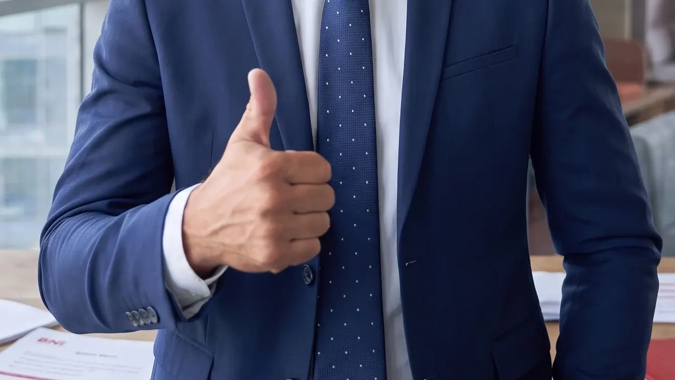 Dłoń z uniesionym kciukiem na tle granatowego garnituru