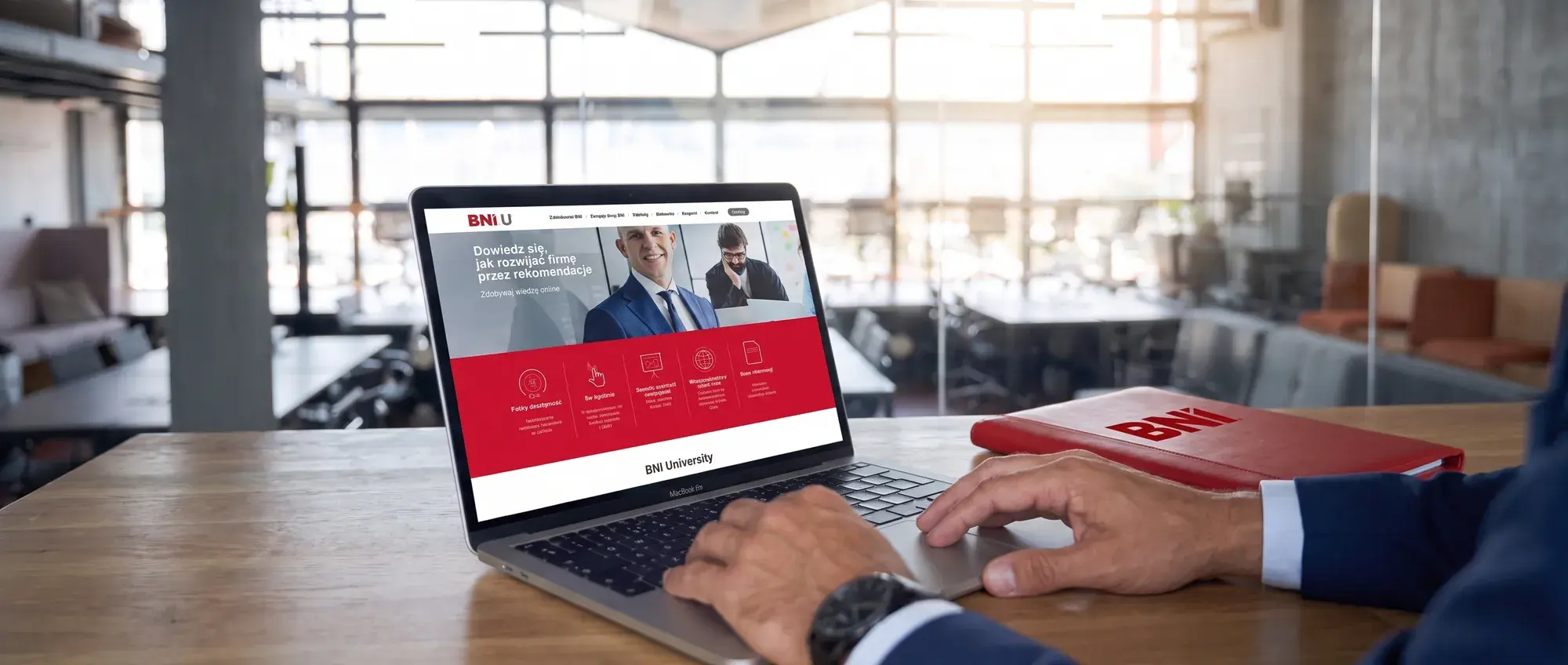 Dłonie na laptopie z platformą BNI University, obok czerwona teczka