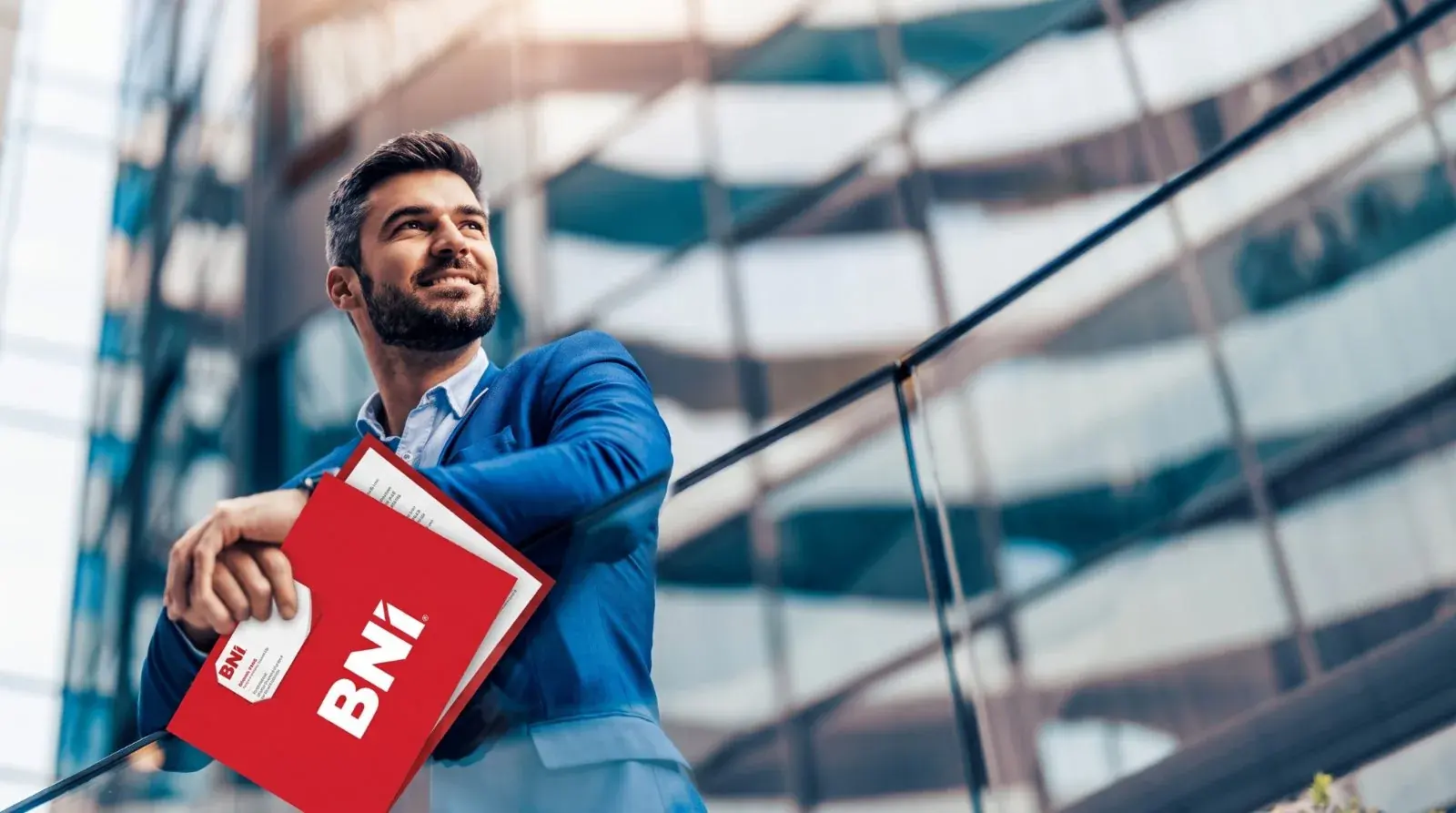 A man in a suit with a red BNI folder in front of a glass-fronted office building