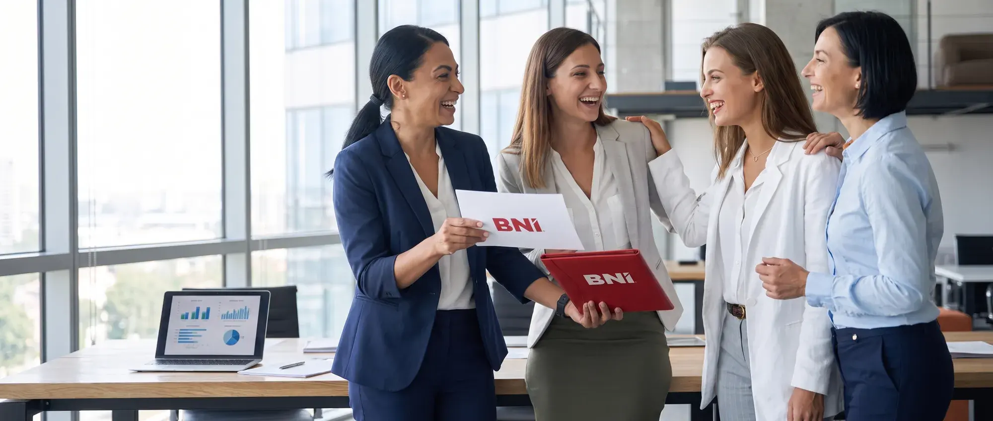 Four laughing women in an office, one holding a red BNI folder