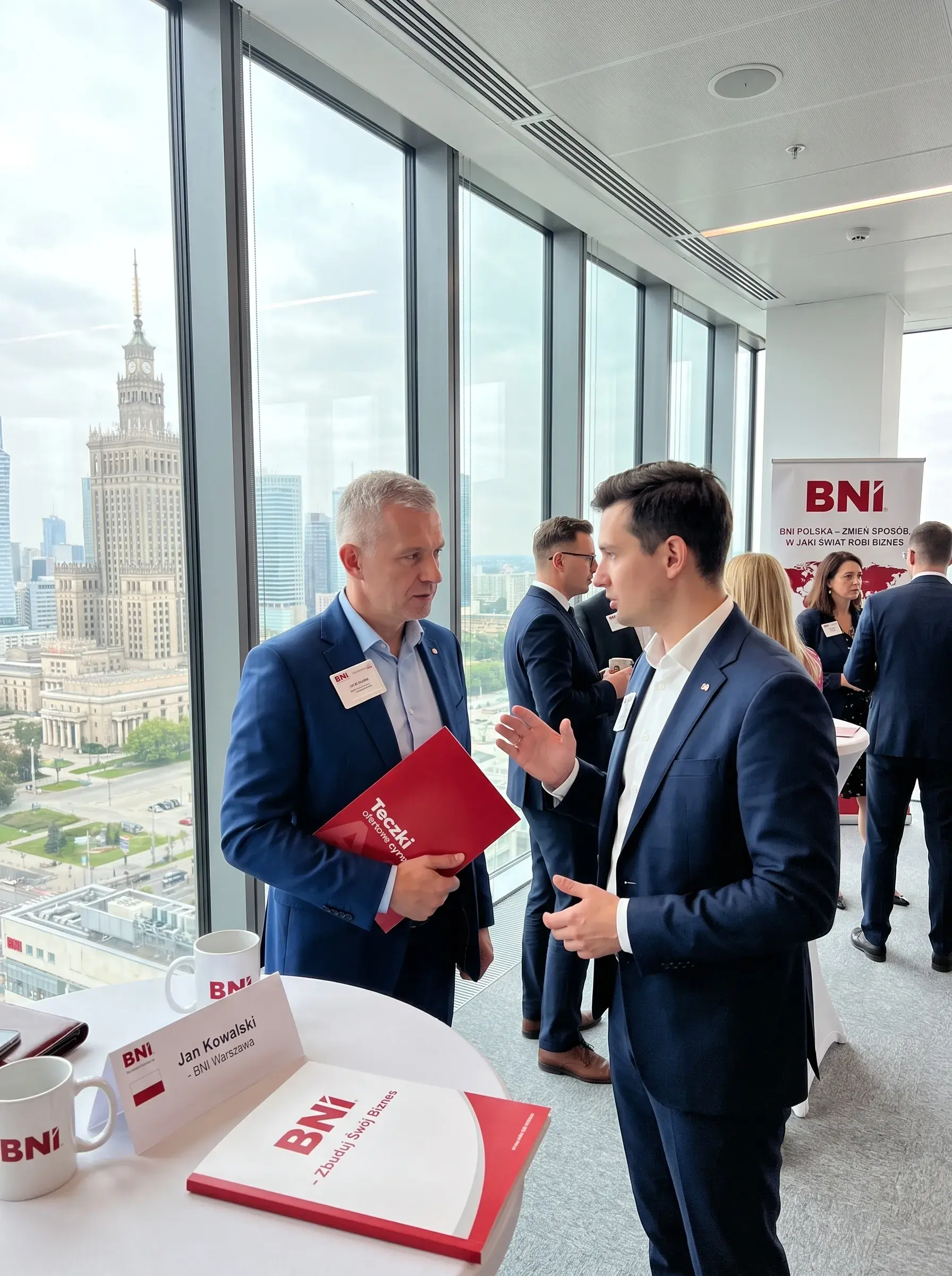 Two men in navy suits talk by a window overlooking the Palace of Culture at a BNI meeting