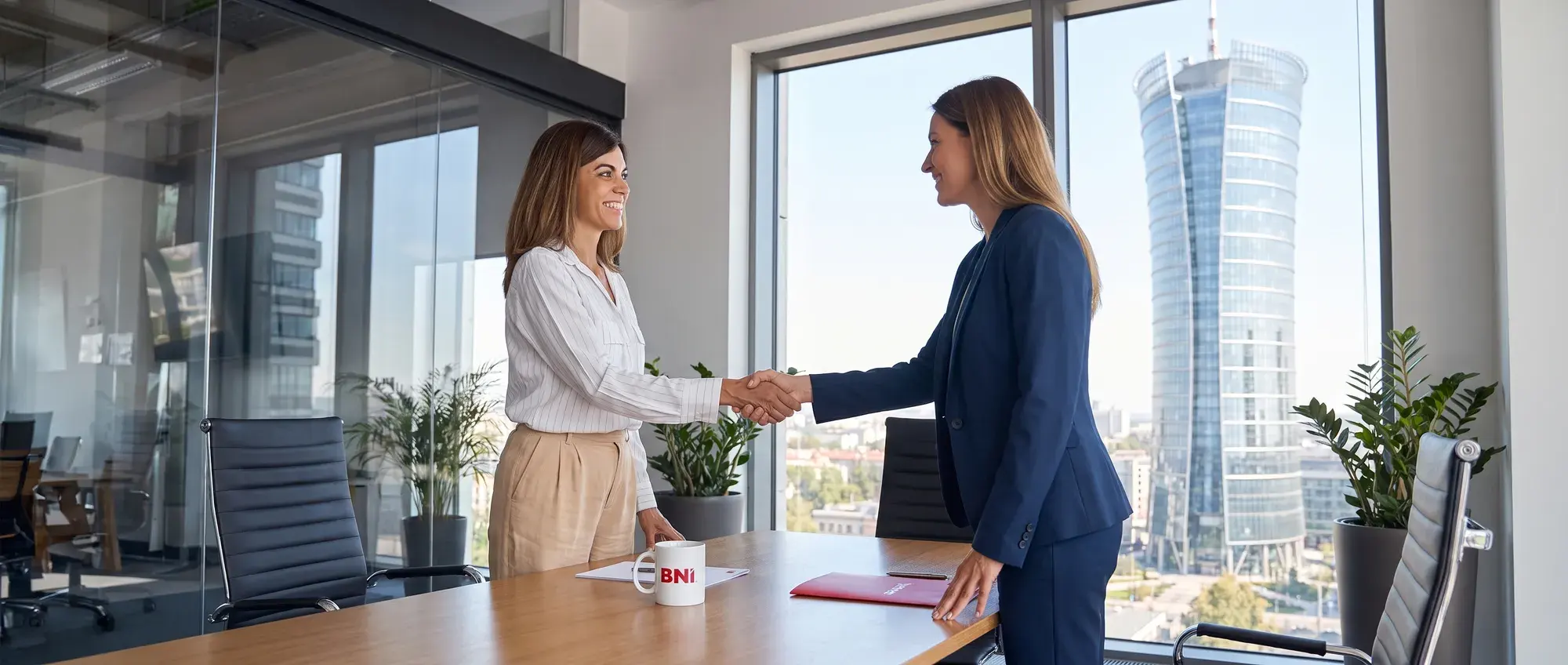 Two businesswomen shake hands in an office overlooking the city