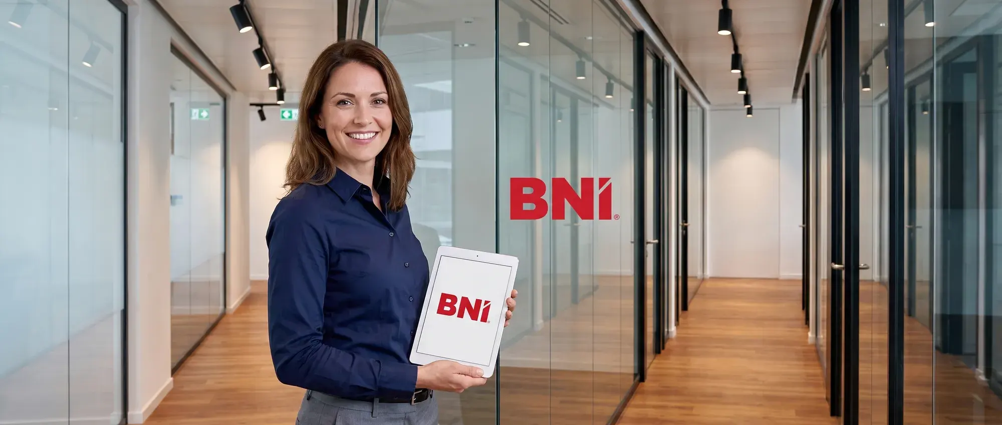 A BNI employee with a tablet smiles in an office corridor