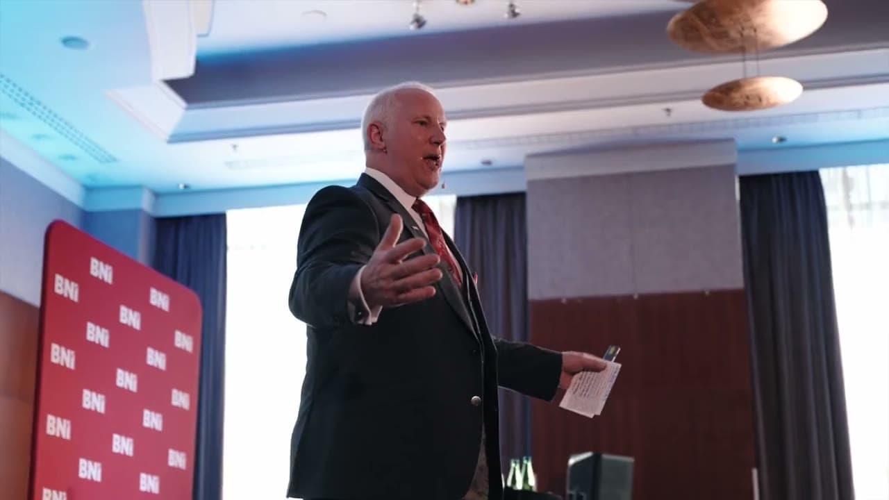 BNI training: the trainer speaks to participants in front of a red BNI wall