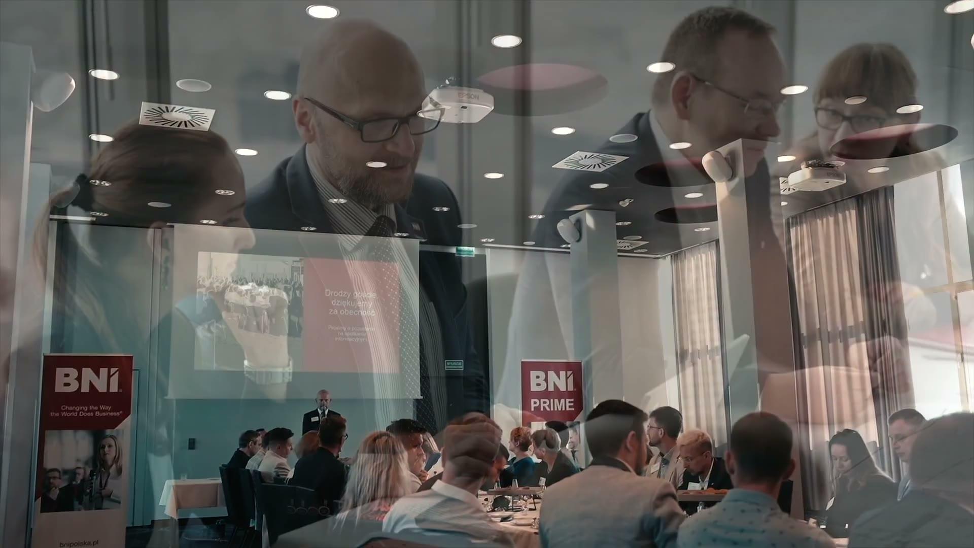 Looping footage from a BNI Chapter Meeting: the room, conversations at the table, a Member speaking with a microphone, applause.