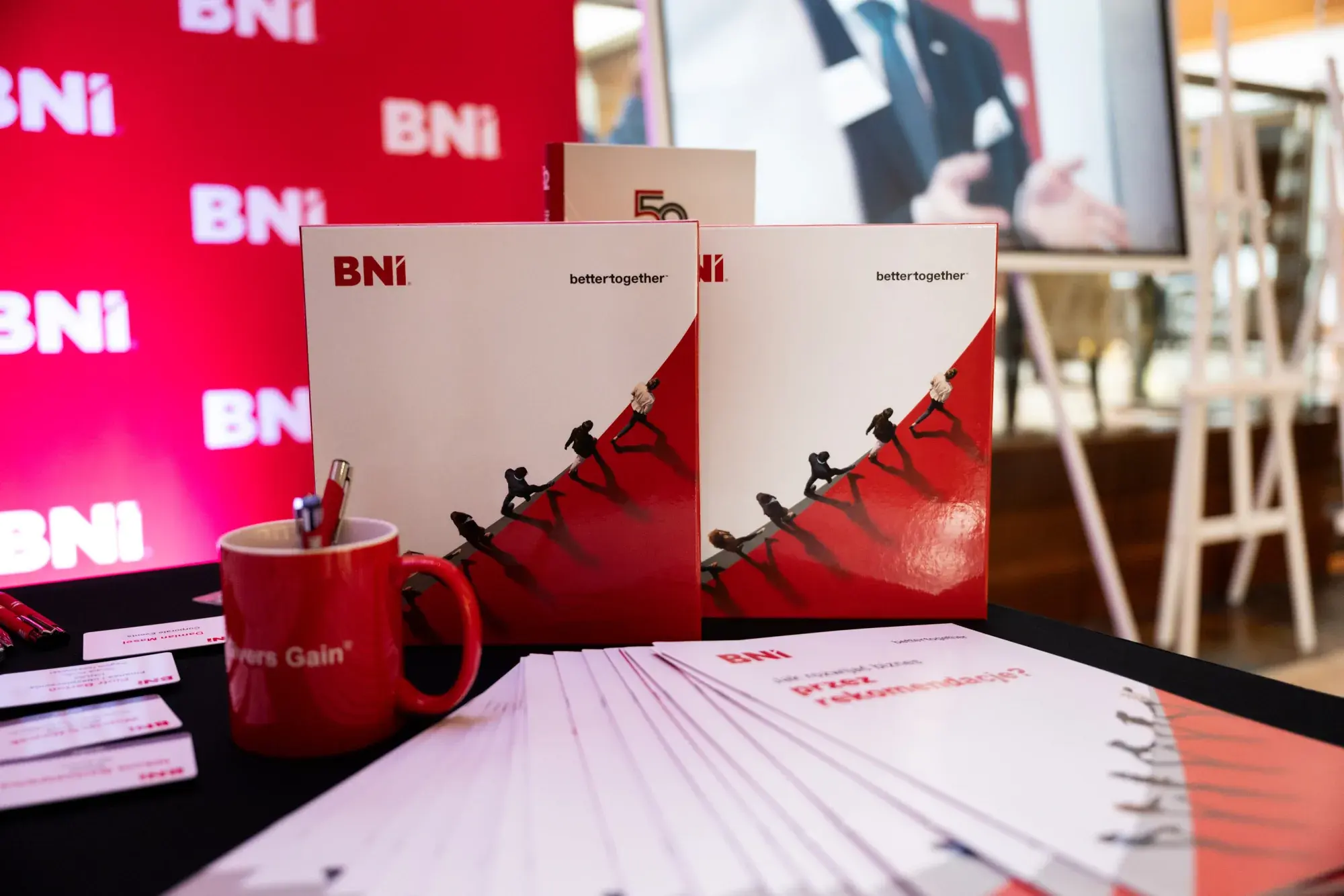 A Givers Gain® mug, folders and BNI materials on a red table before a Chapter Meeting